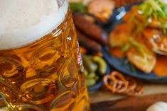 a glass of beer sitting on top of a wooden table next to plates of food