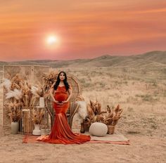 a pregnant woman in an orange dress standing next to a basket with wheat on it