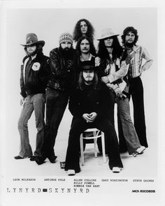 an old black and white photo of a group of people with long hair, standing in front of a chair