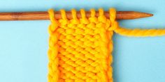 an orange crochet stitch being worked on with a wooden knitting needle in the foreground