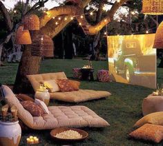 an outdoor movie is set up in the grass with lights strung over it and pillows on the ground