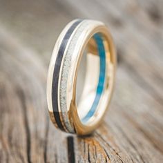 a wedding ring with two blue and white stripes on it sitting on top of a wooden table