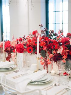 the table is set with red flowers and candles