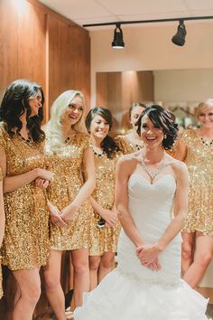 a group of women standing next to each other in front of a mirror wearing gold dresses