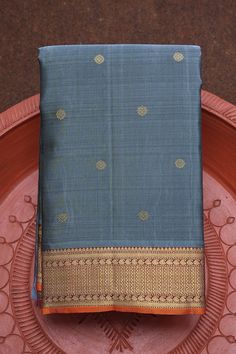 This handwoven Kanchipuram Silk Saree in steel blue has floral buttis in body with contrast border in maroon. The border houses chevron and paisley design in gold zari. It is completed with orange selvedge and the pallu features traditional design in zari. Includes unstitched blouse piece. Silk Sarees Kanchipuram, Fashionable Saree, Kanchi Sarees, Blue Silk Saree, Silk Saree Kanchipuram, Dobby Fabric, Saree Silk, Wedding Silk Saree