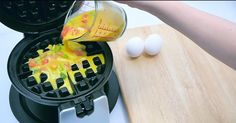 a person pouring orange juice into a waffle iron on a cutting board next to eggs