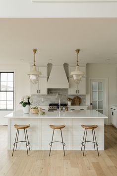 two stools sit in front of an island with white countertops and cabinets,