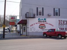 a red truck is parked in front of a building with a sign for helio's body shop