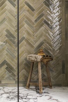 a wooden stool sitting in front of a tiled wall