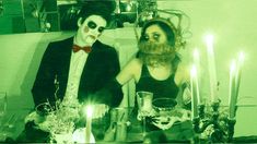 two people dressed up in costumes sitting at a table with candles and plates on it