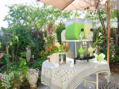 a table with an umbrella and vases on it in the middle of a garden