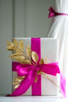 a white gift box with pink ribbon and gold leaf decoration