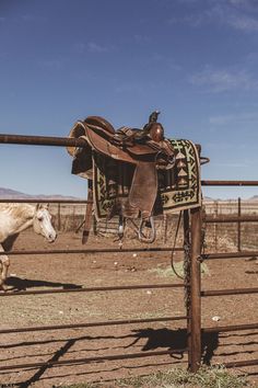 a saddle hanging on a fence with a horse in the back ground and another horse behind it