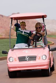 two people riding in a pink golf cart