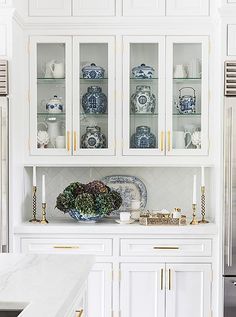 a kitchen with white cabinets and blue and white dishes on the counter top, along with gold trimmings