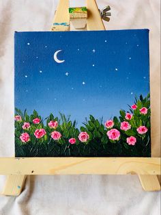 an easel with flowers painted on it and a moon in the sky above them