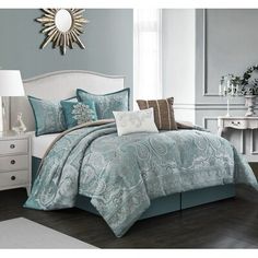 a bed with blue and white comforters in a room next to a dresser, mirror and lamp