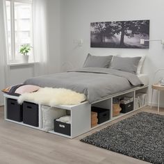 a bed with storage boxes underneath it in a white room next to a rug and window