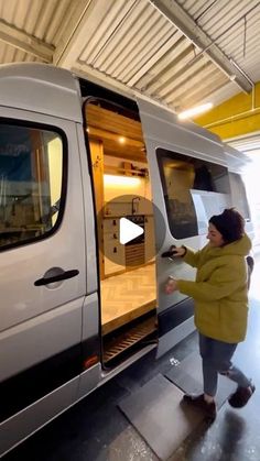 a woman standing next to a van in a garage with the door open and it's doors wide open