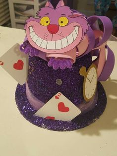 a purple hat with a cat on top and playing cards in the bottom, sitting on a table