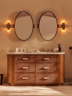 two round mirrors are mounted on the wall above a vanity with drawers and lights around it