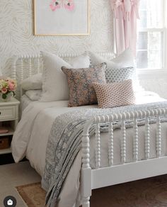 a white bed sitting in a bedroom next to a window with pink flowers on it