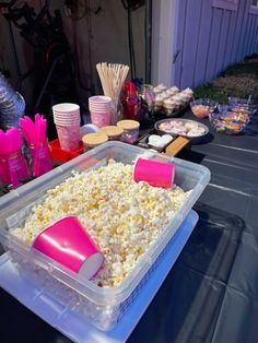 a plastic container filled with popcorn sitting on top of a table next to other food