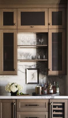 a kitchen with wooden cabinets and white marble counter tops, wine glasses on the shelves