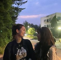 two young women standing next to each other on the side of a road at night