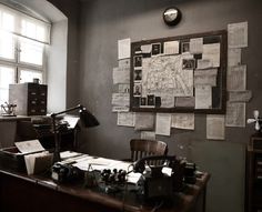 an old fashioned desk with lots of papers on it and a lamp in the corner