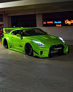 a green sports car parked in front of a parking garage with neon signs behind it