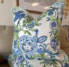 a blue and green floral pillow sitting on top of a couch next to a wall