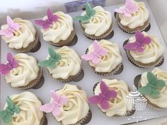 there are many cupcakes with white frosting and pink flowers on them in the box