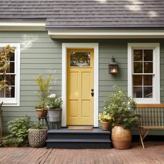 a yellow door sits in front of a gray house with potted plants on the porch