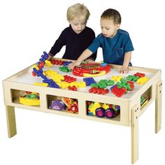 two young boys playing with toys in a play table on a white background, one boy is looking at the toy