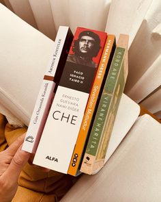 a stack of books sitting on top of a white couch next to a person's hand