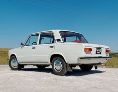 an old white car is parked on the gravel