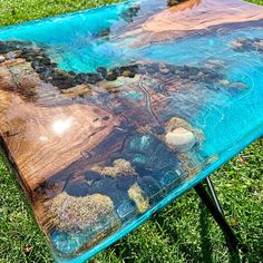 a table made out of wood and glass in the grass with blue paint on it