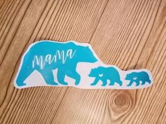 a mama bear and two cubs sticker on a wooden surface with the word mama written in blue