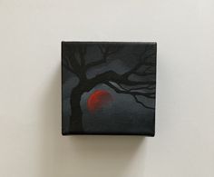 a small square painting with a red moon in the sky and tree branches on it