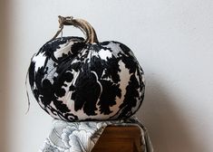 a decorative black and white pumpkin sitting on top of a wooden box next to a wall