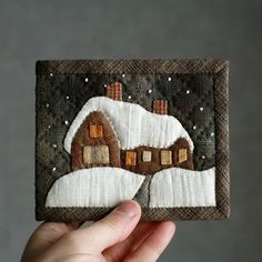 a hand holding up a small piece of art that looks like a house in the snow