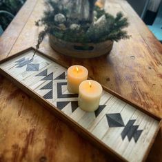 two candles sitting on top of a wooden table next to a potted plant and candle holder