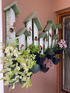 several birdhouses are lined up on the wall with plants in them and hanging from it's sides