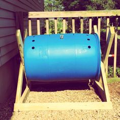 a large blue barrel sitting on top of a wooden stand next to a building with trees in the background