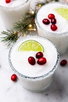 two margaritas with cranberries and lime on the rim are garnished with christmas greenery