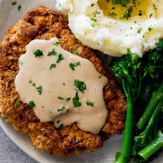 a plate topped with fried chicken, mashed potatoes and broccoli covered in gravy