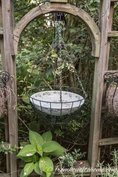 a bird feeder hanging from the side of a wooden trellis with plants growing in it