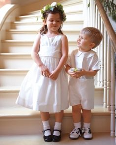 two young children standing next to each other in front of some stairs with flowers on their head