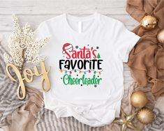 Santa's Favorite Cheerleader T-shirt, Cheerleader Holiday Women Shirt, Cute Cheer Player Christmas Tee, Funny Cheerleader Christmas Gift 1. Check our photos for sizing and color options.  2. Choose your quantity. Feel free to add as many shirts as you wish!  3. Select your size and color from the drop-down menus.  4. Click "ADD TO CART" to add the shirt to your virtual cart.  5. Click "PROCEED TO CHECKOUT" to purchase your shirt.  6. Your shirt is now off to production! We will process your order and your shirt will be ready for shipment in 1-4 days!  **SHIRT SIZING** All of our shirts come in a variety of colors and many different sizes! **PROCESSING & SHIPPING** Your order should take approximately 3-7 business days to arrive at your door! Generally, the process and shipping time is as f Cheerleader Christmas Gifts, Funny Cheerleader, Cheerleading Shirts, Pom Pom Girl, Girl T Shirt, Women Shirt, Christmas Tees, Christmas Shirts, Cheerleading